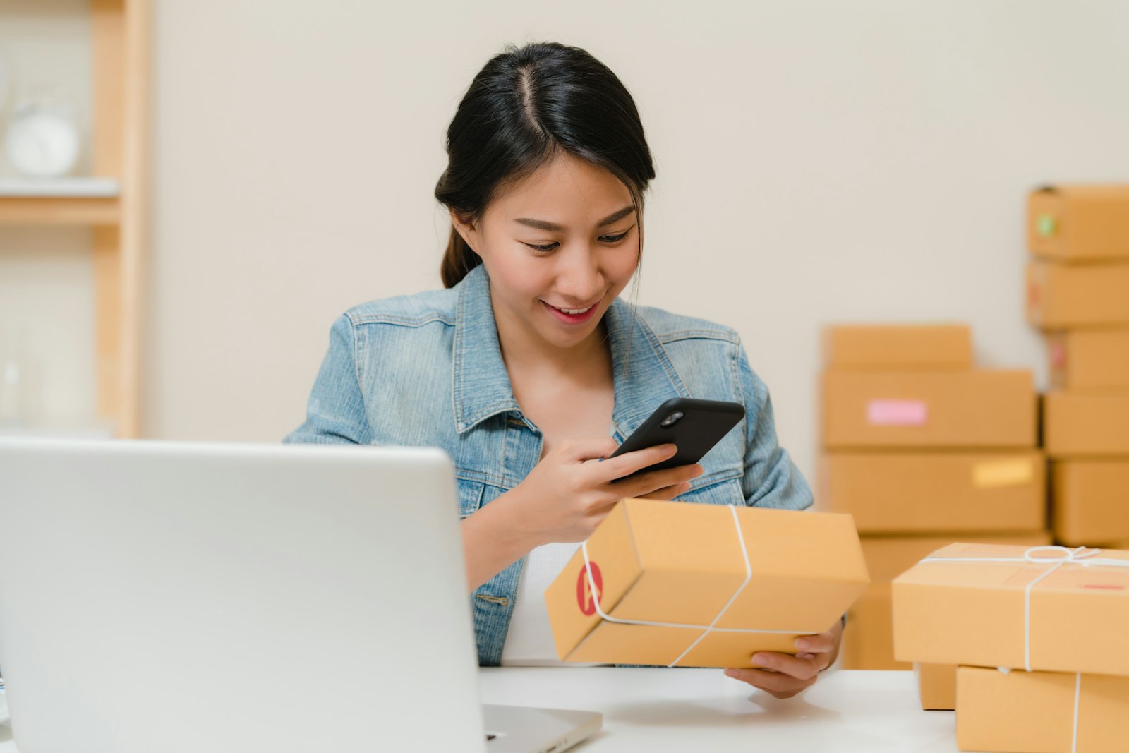 Pemilik usaha online tersenyum memotret paket pesanan di antara tumpukan kardus