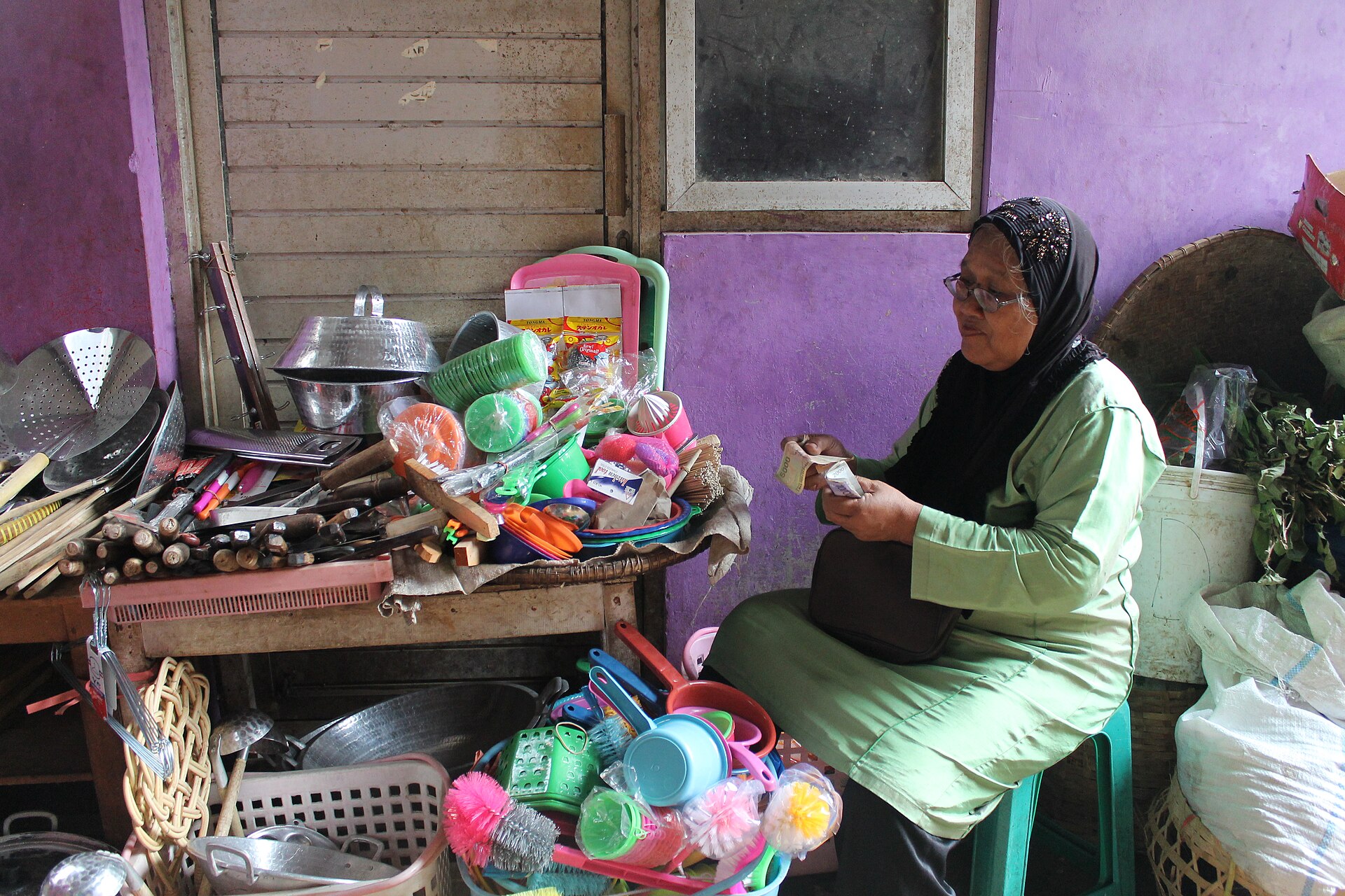 Pedagang perabotan di Pasar Wage, Purwokerto, menghitung penghasilan sejak pagi. Foto: Dhita Gustiani, Wikimedia Commons, CC BY-SA 4.0